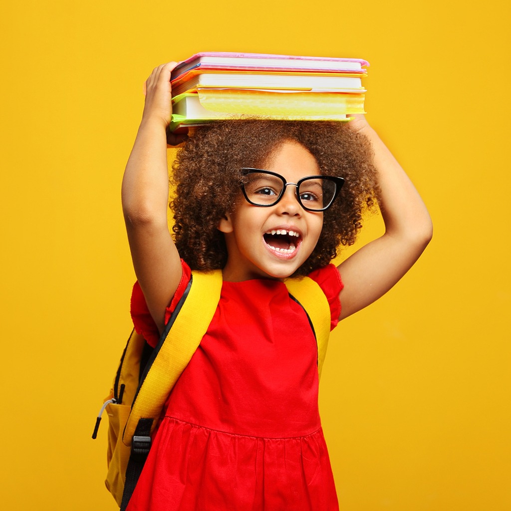A cheerful girl with curly hair and glasses, balancing books on her head, wears a red dress and a yellow backpack against a bright yellow backdrop.